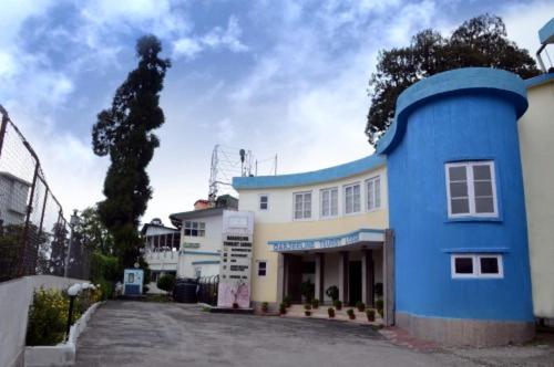 un bâtiment bleu avec un arbre devant lui dans l'établissement Darjeeling Tourist Lodge, à Darjeeling