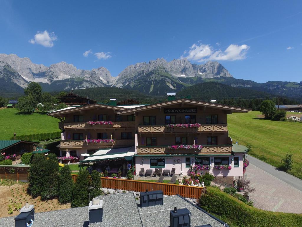 a large building with mountains in the background at Pension Sunnberg in Going am Wilden Kaiser