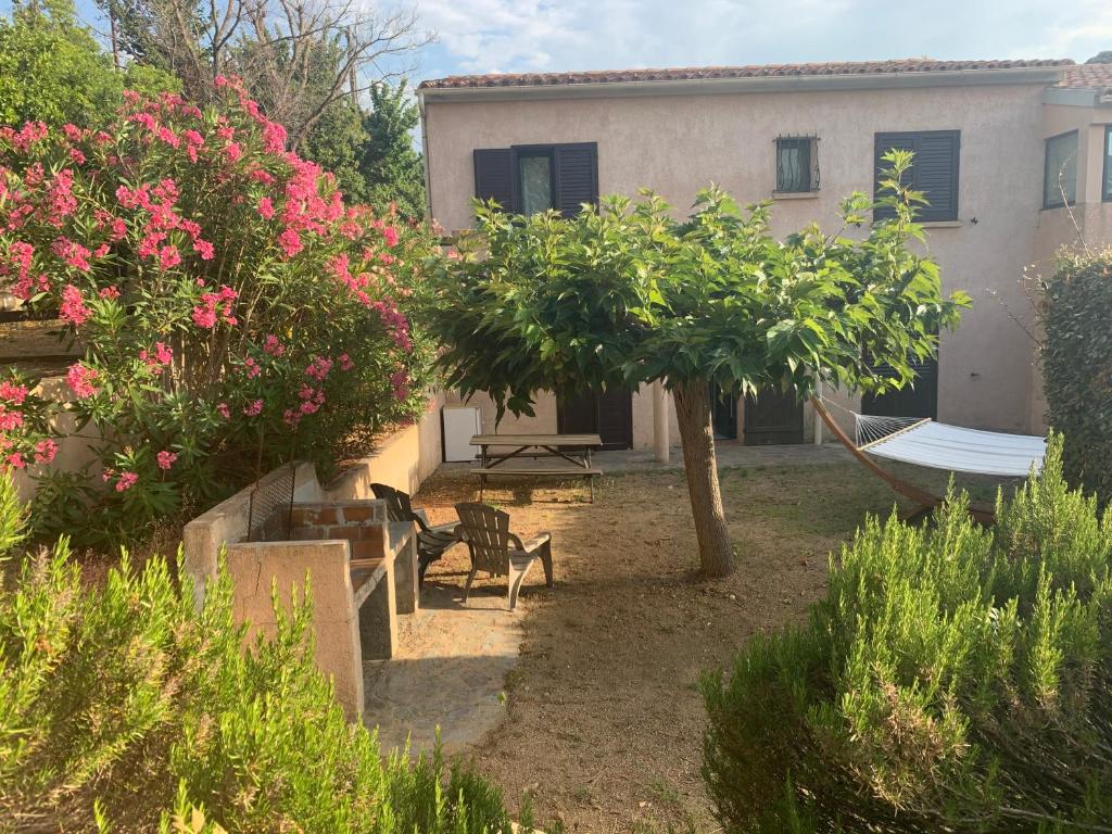 ein Haus mit einem Garten mit rosa Blumen und einer Hängematte in der Unterkunft Chambres et tables d'hôtes Zélia & Jacques BERQUEZ in Pianottoli-Caldarello