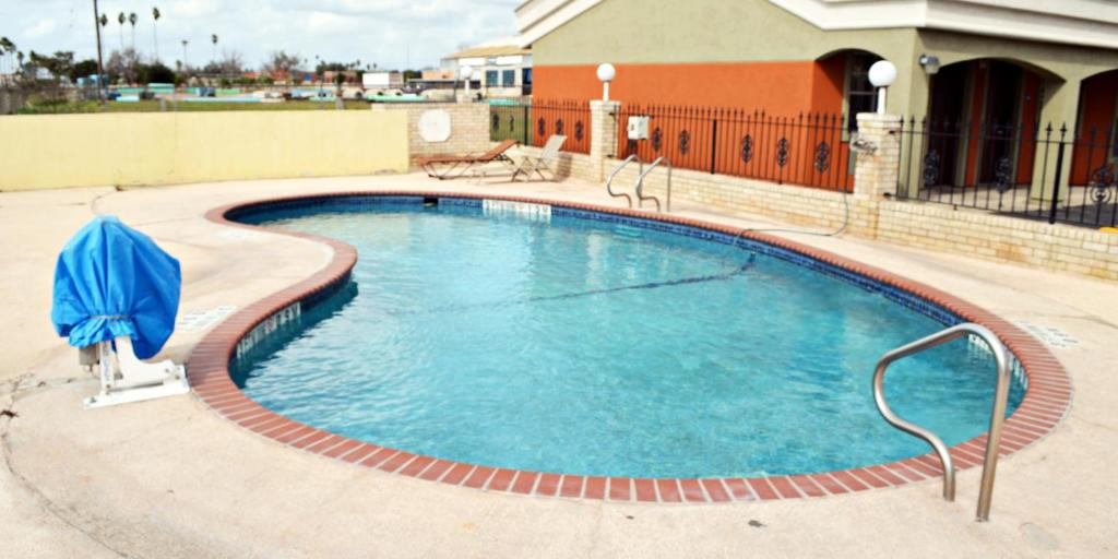 una gran piscina con sombrilla azul frente a un edificio en Aloha Inn, en McAllen