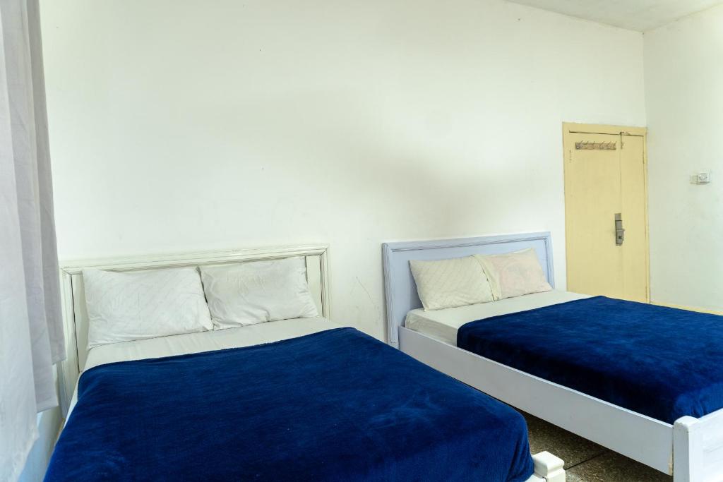 2 bedden in een witte kamer met blauwe lakens bij Brannic Lodge in Accra