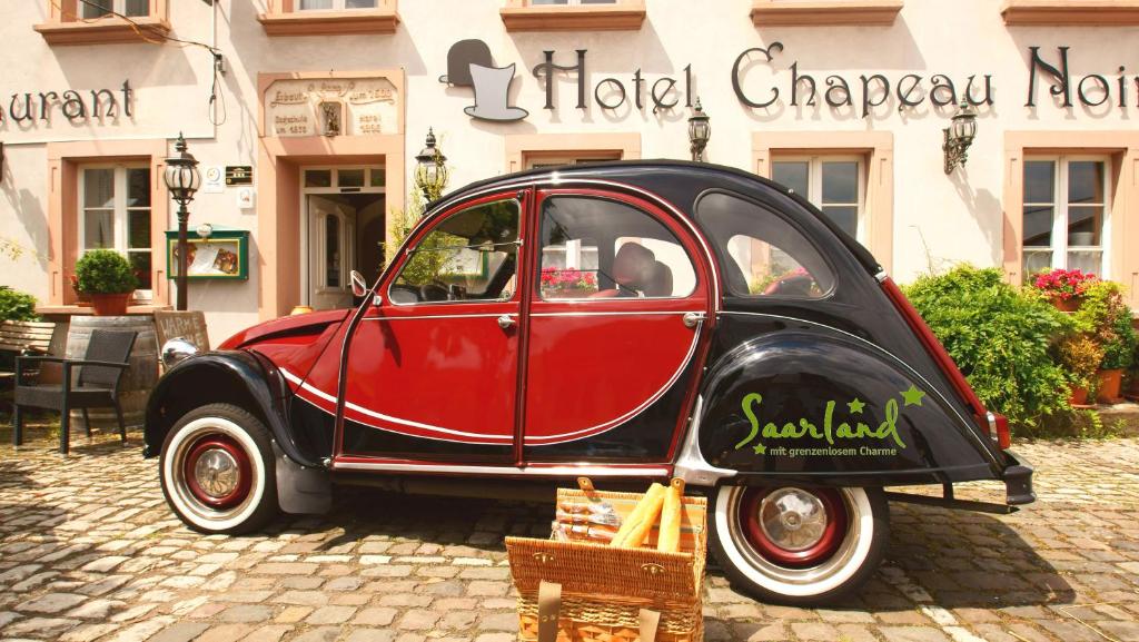 une voiture rouge et noire garée devant un bâtiment dans l'établissement UNO Hotel Chapeau Noir, à Überherrn
