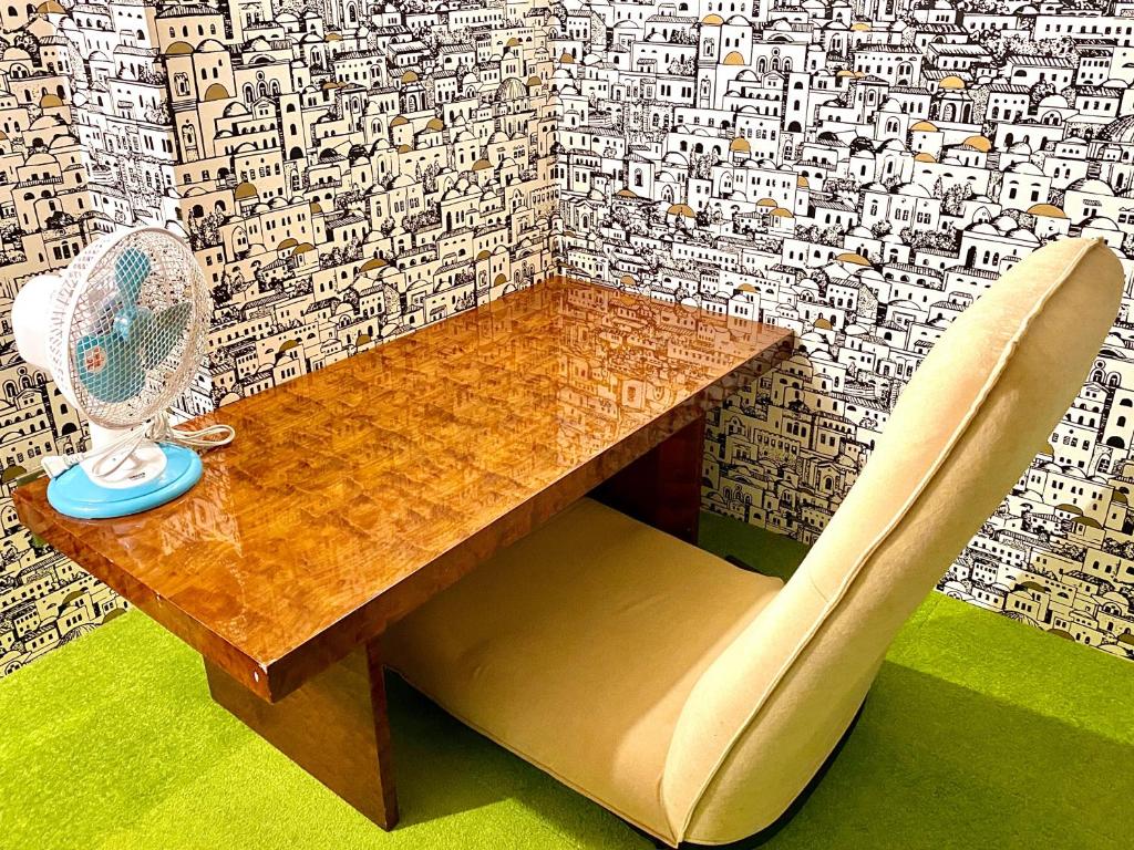 a table and a chair with a fan and a wall at Guest House MARUYA in Atami