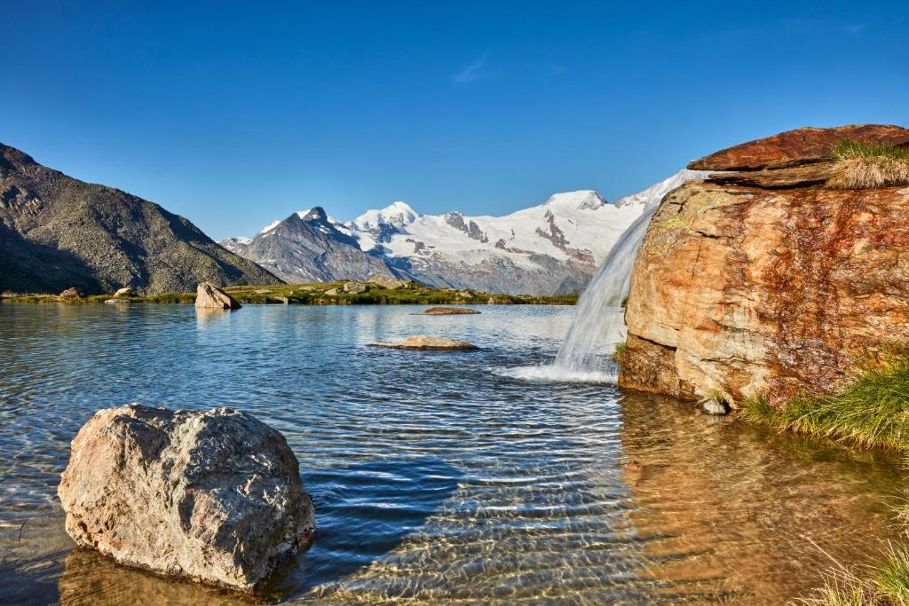 a waterfall in a lake with mountains in the background at Sunshine in Saas-Grund