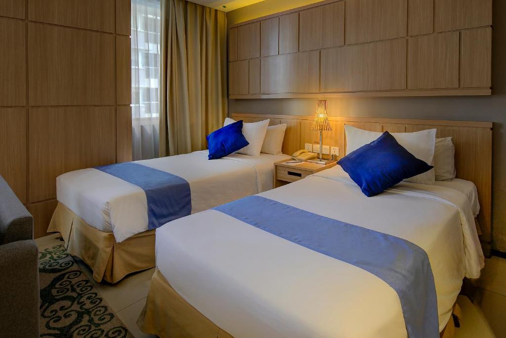 two beds in a hotel room with blue pillows at Golden Tulip Balikpapan Hotel & Suites in Balikpapan