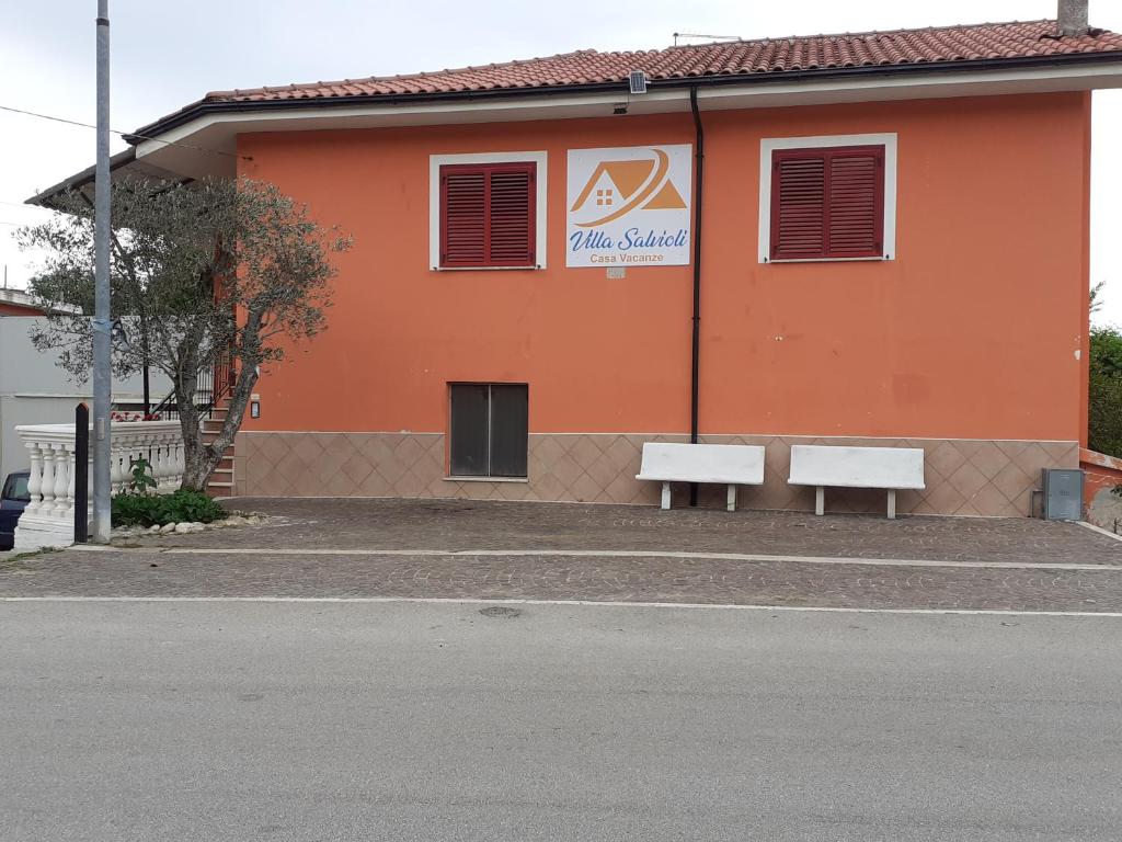 een oranje gebouw met twee banken ervoor bij Villa Salvioli in San Rufo