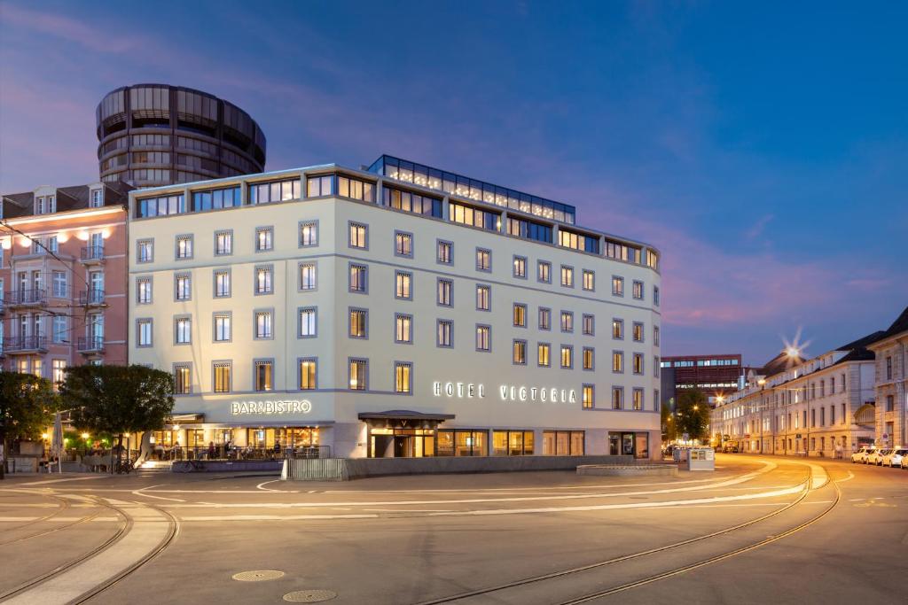ein großes weißes Gebäude in der Nacht auf einer Stadtstraße in der Unterkunft Hotel Victoria in Basel
