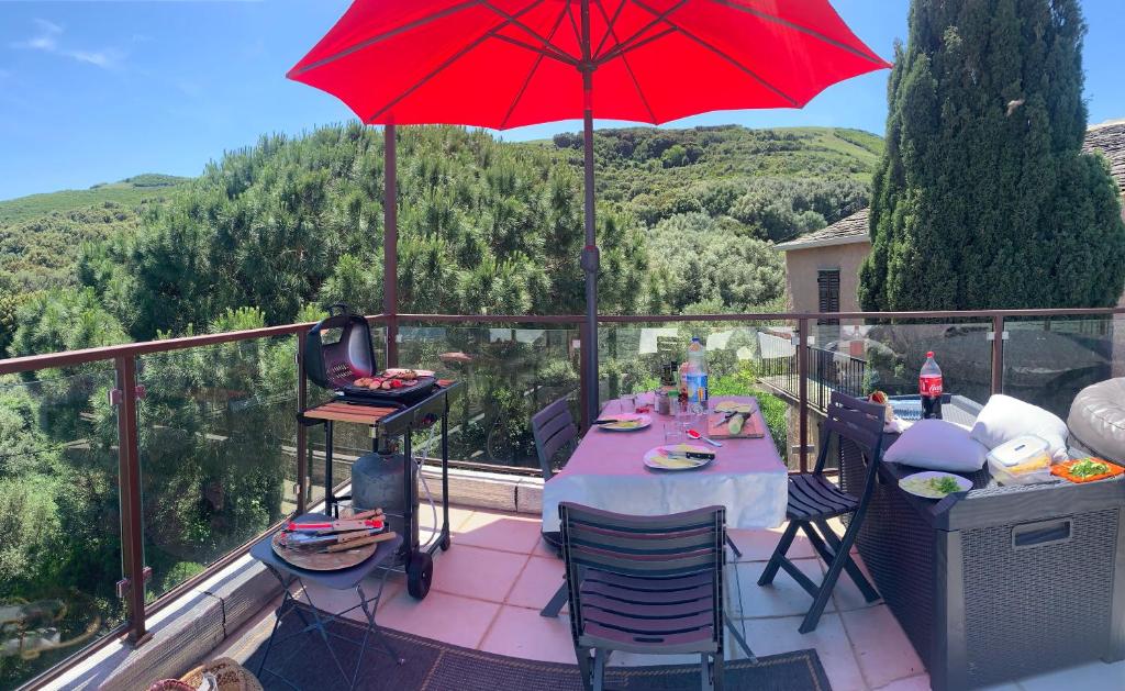 einen Tisch auf einem Balkon mit einem roten Regenschirm in der Unterkunft La charmante **** Maison Cap Corse, Tomino in Mandolacce