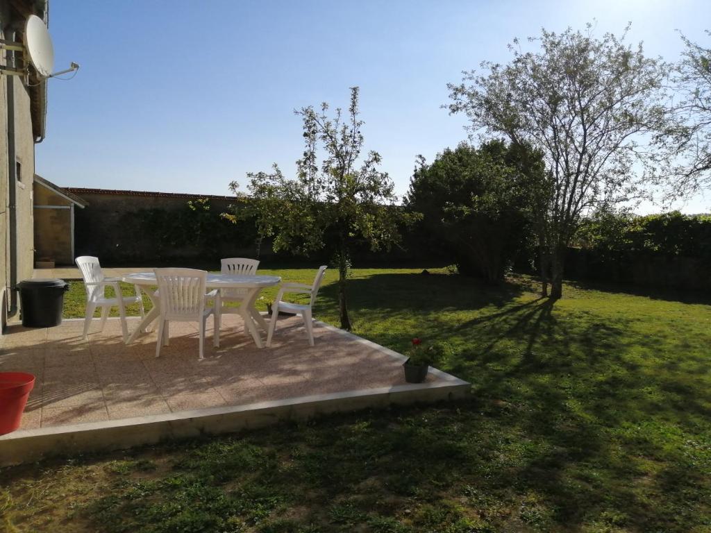 a patio with white chairs and a table in a yard at Gîte de la Bigaillonne in Saint-Marcel