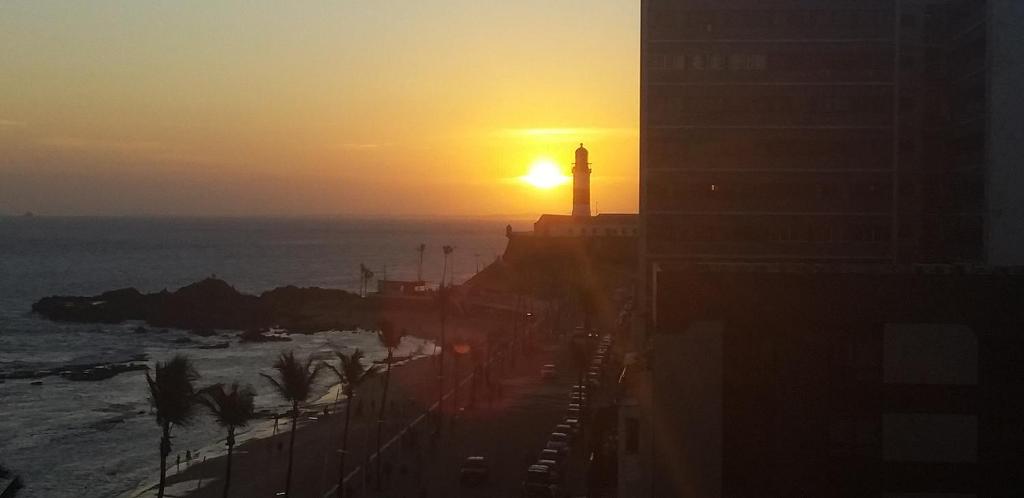 una puesta de sol sobre el océano con un faro en la distancia en Apartamento Farol Barra Flat, en Salvador