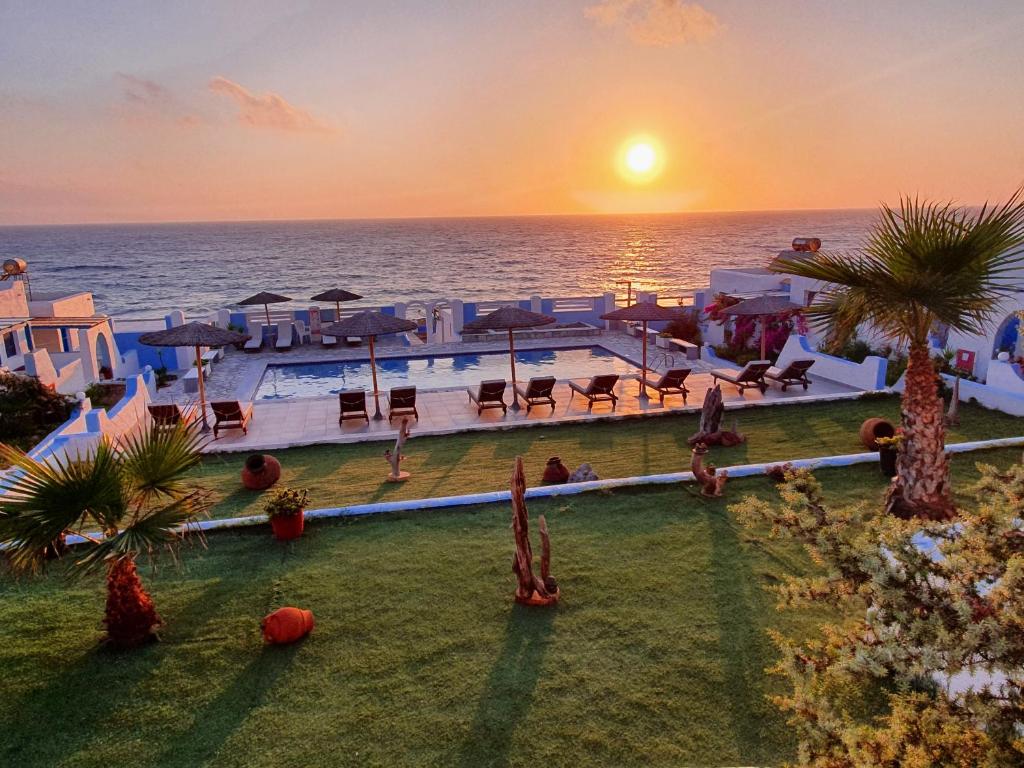 a resort with a pool and the ocean at sunset at Elenis Studios in Arkasa