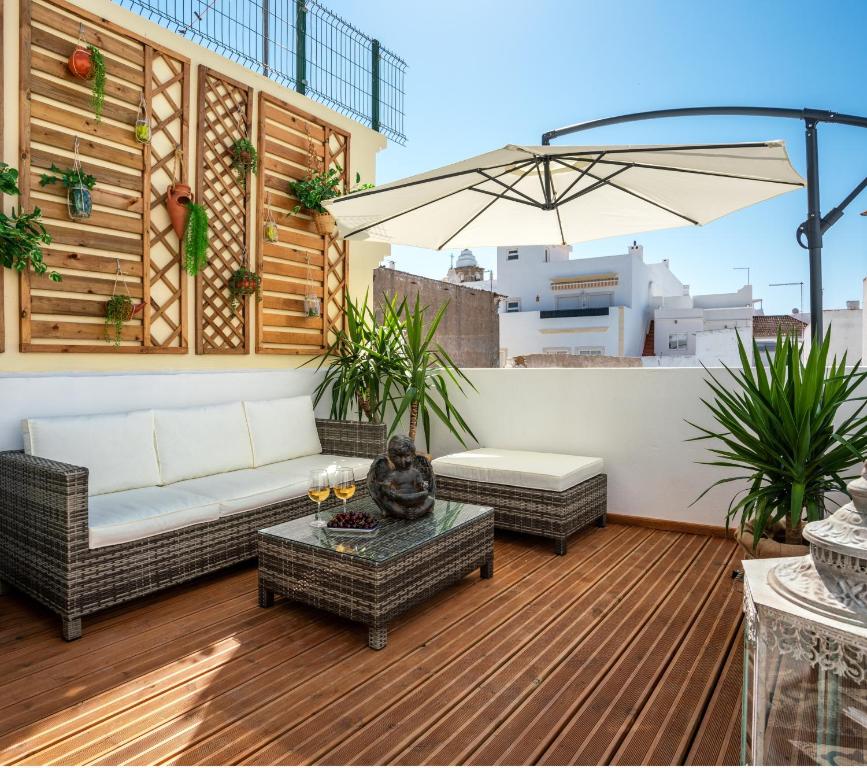 eine Terrasse mit einem Sofa, Tischen und einem Sonnenschirm in der Unterkunft CASA DA AVO by Ammonite&Co in Olhão