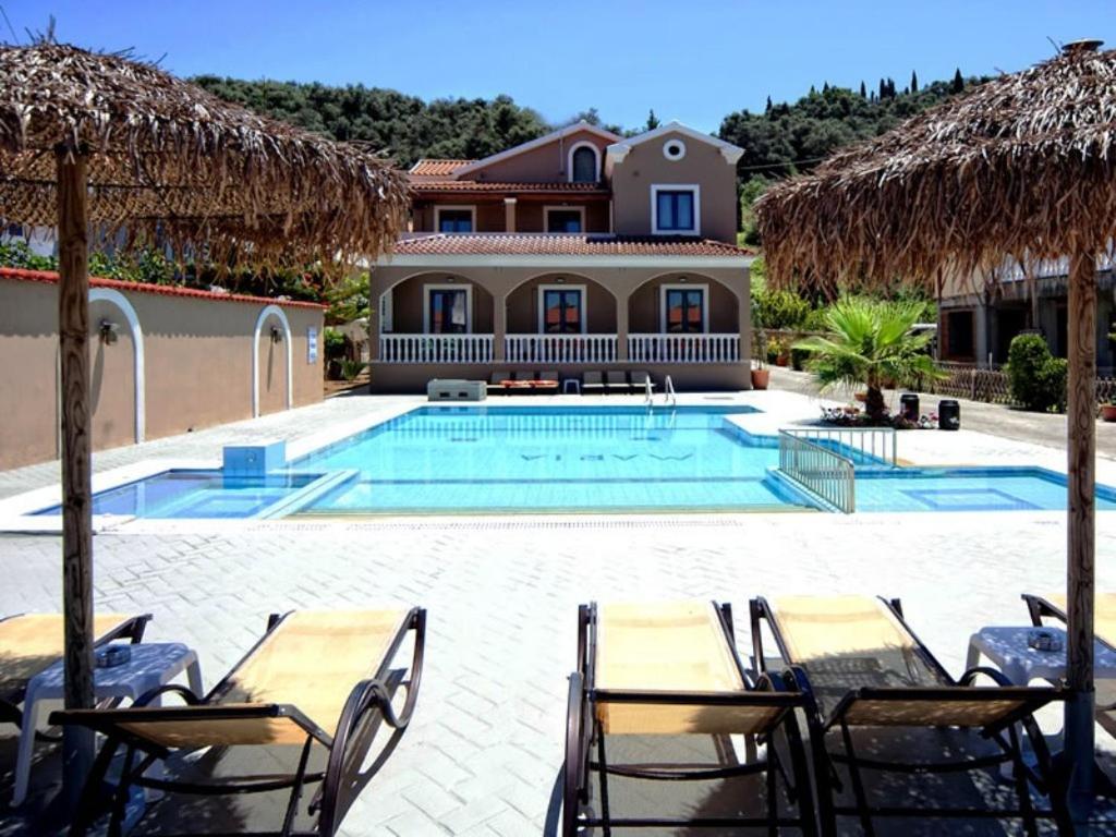 a swimming pool with tables and chairs and a house at Maria Apartments in Sidari