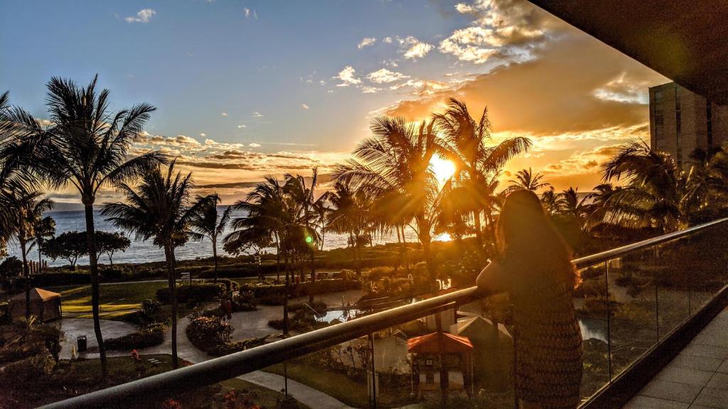 a woman standing on a balcony watching the sunset at Honua kai - Konea 301 Frontline with BBQ! in Kaanapali