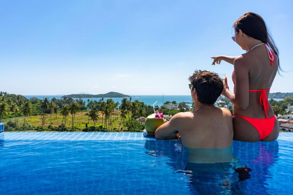 a woman and a man sitting on the edge of a swimming pool at Babylon Sky Garden - Long Term Holiday Rentals in Rawai Beach