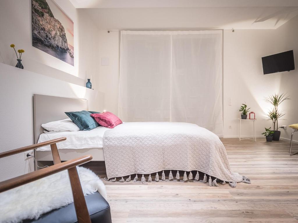 Dormitorio blanco con cama con almohadas rosas y azules en Freiburger-Ferienwohnung, en Freiburg im Breisgau