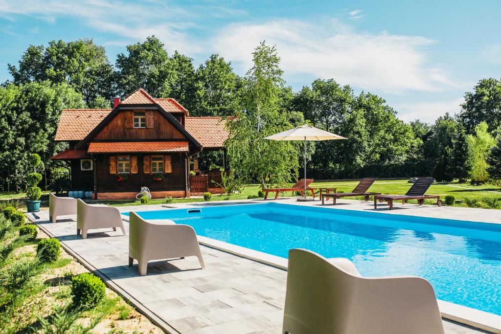a pool with chairs and a house in the background at Moslavačka Priča Holiday Homes in Mala Ludina
