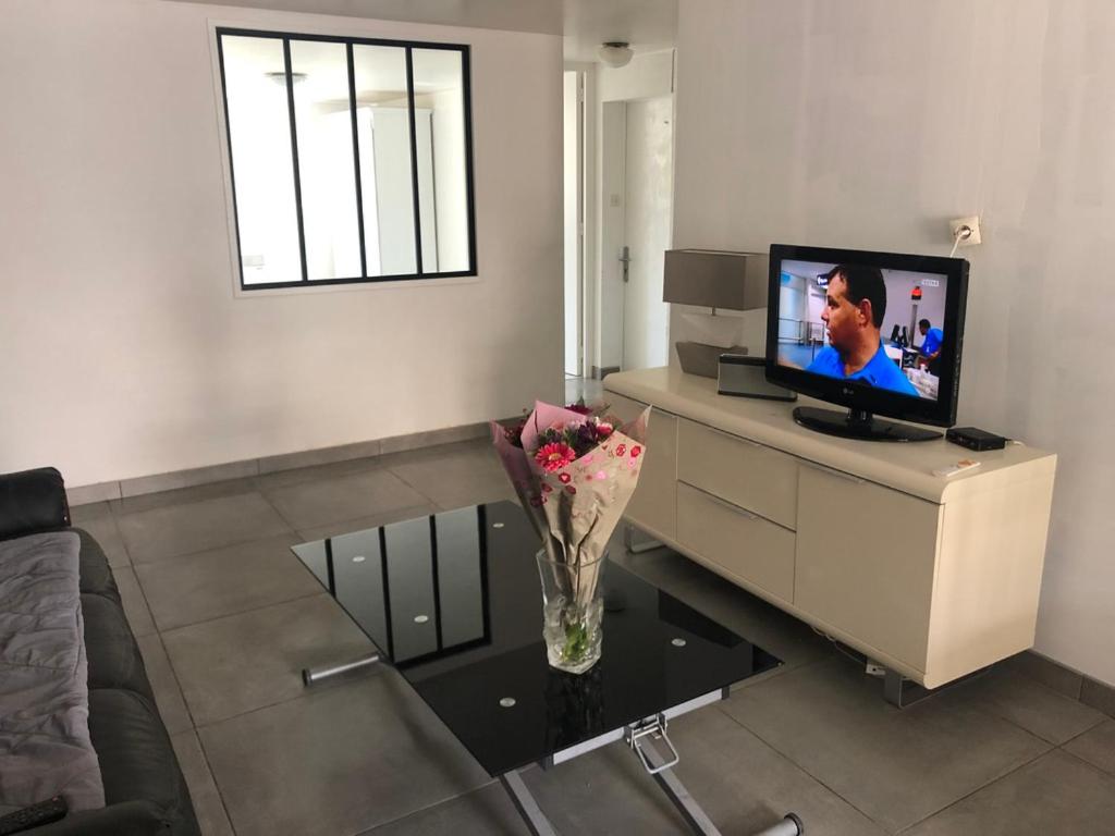 ein Wohnzimmer mit einem TV und einer Vase aus Blumen auf dem Tisch in der Unterkunft 61 BIS ST GEORGES DE DIDONNE in Saint-Georges-de-Didonne