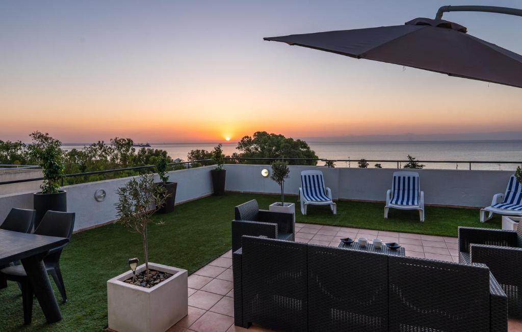 eine Terrasse mit Stühlen, einem Sonnenschirm und dem Meer in der Unterkunft MAKENZY Seaview PENTHOUSE in Larnaka