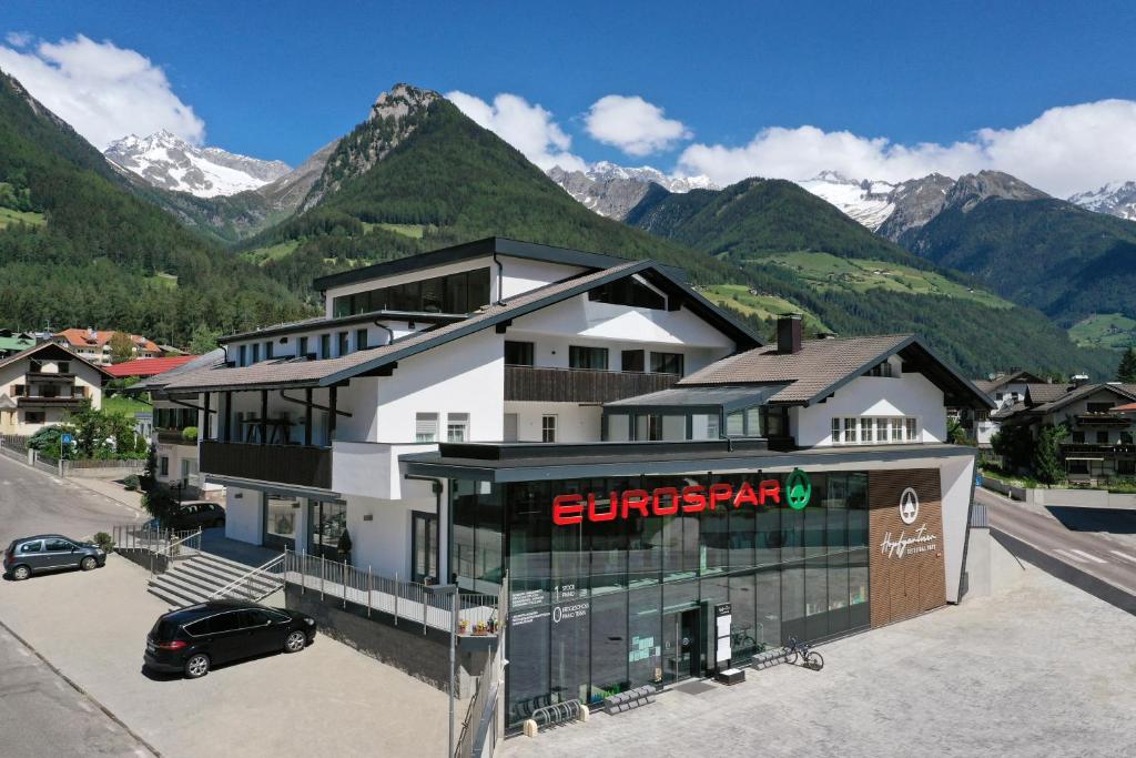 a building with a car parked in front of a mountain at Appartments Hopfgartner Eurospar in Lutago