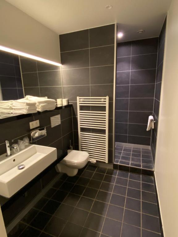 a bathroom with a toilet, sink, and mirror at Hotel New Regina in Ieper