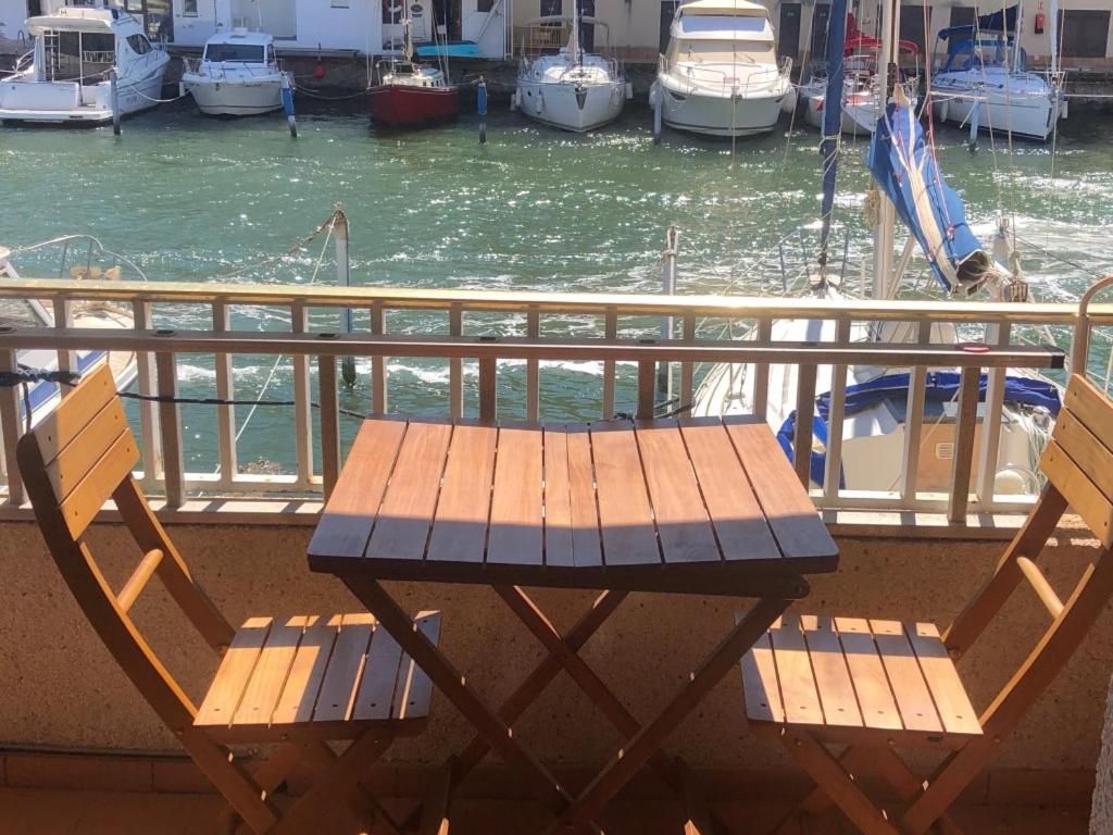 una mesa de madera y 2 sillas en un balcón con barcos en PORT AMBAR - Apartamento en la Marina de Empuriabrava - balcón con vistas al canal - playa - wifi, en Empuriabrava