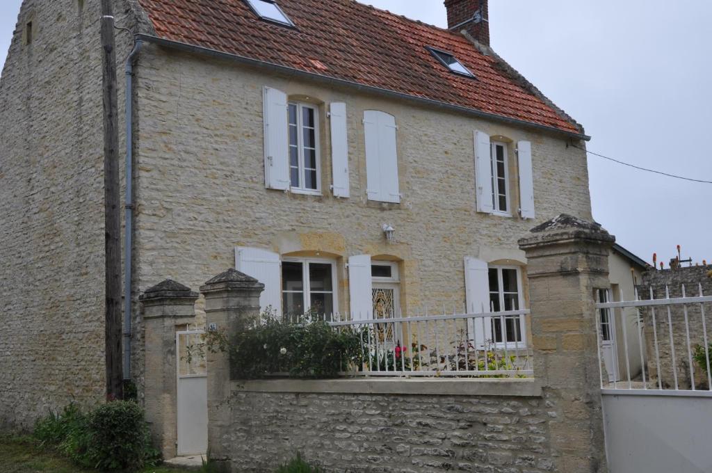 una vieja casa de ladrillo con una valla blanca en Le petit clos du Bessin en Longues-sur-Mer