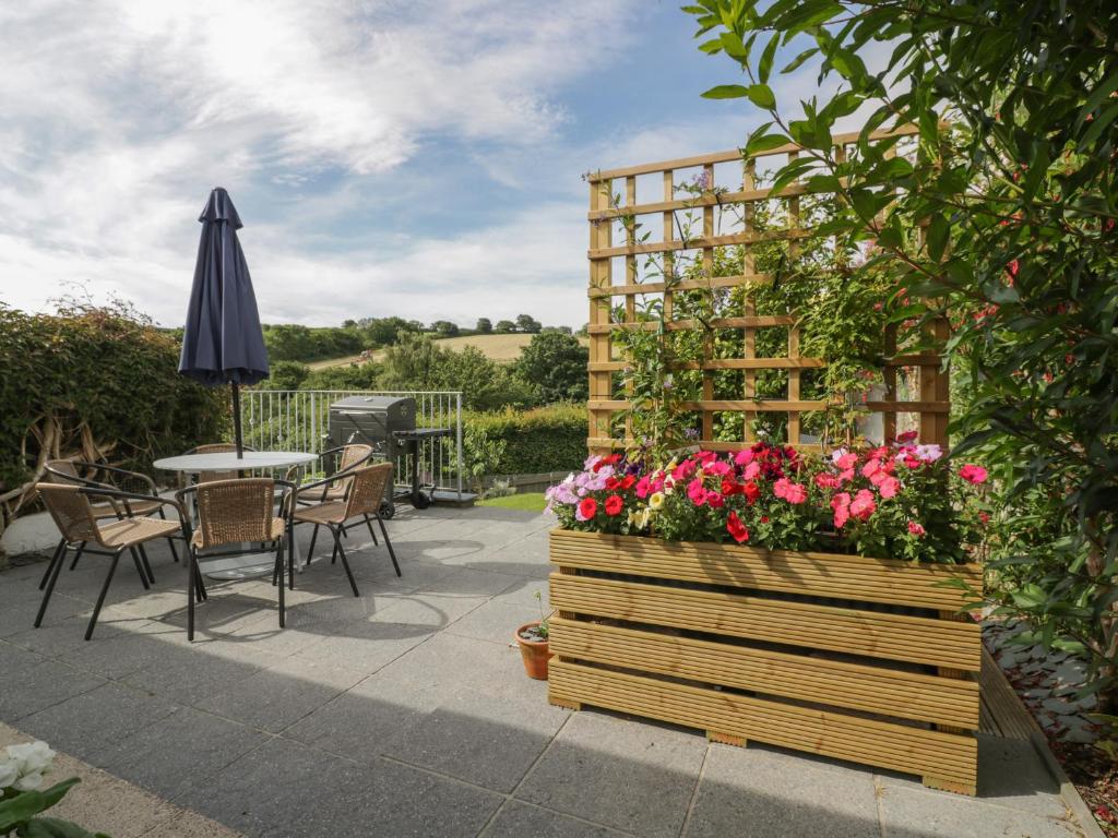 a patio with a table and an umbrella and flowers at Orchard View in St Austell