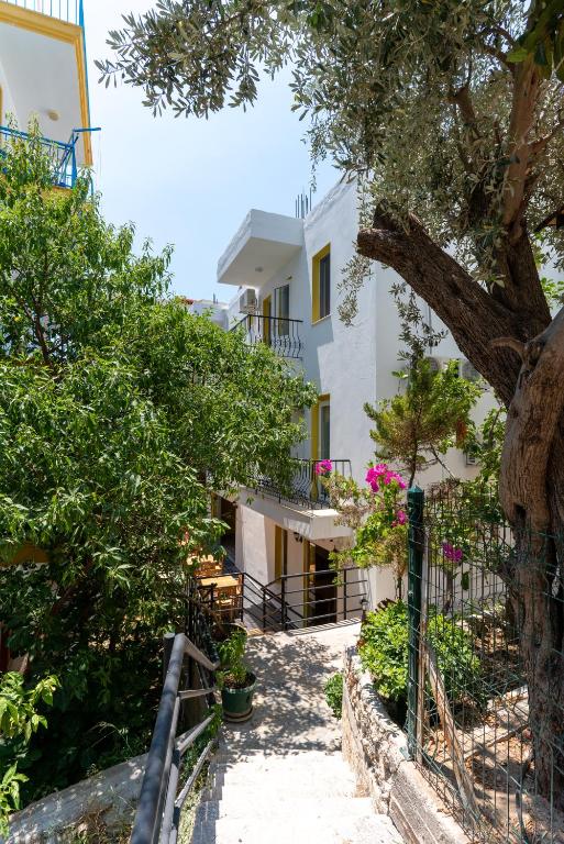 a walkway leading to a white building with trees at Holy Pansiyon in Kaş