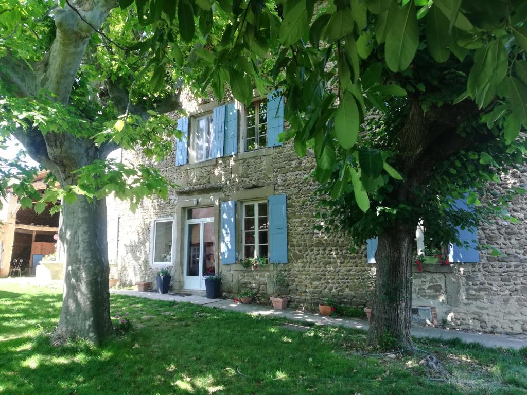 una antigua casa de piedra con persianas azules y árboles en STUDIO INDEPENDANT DANS FERME 18ème en Saint-Michel-sur-Savasse