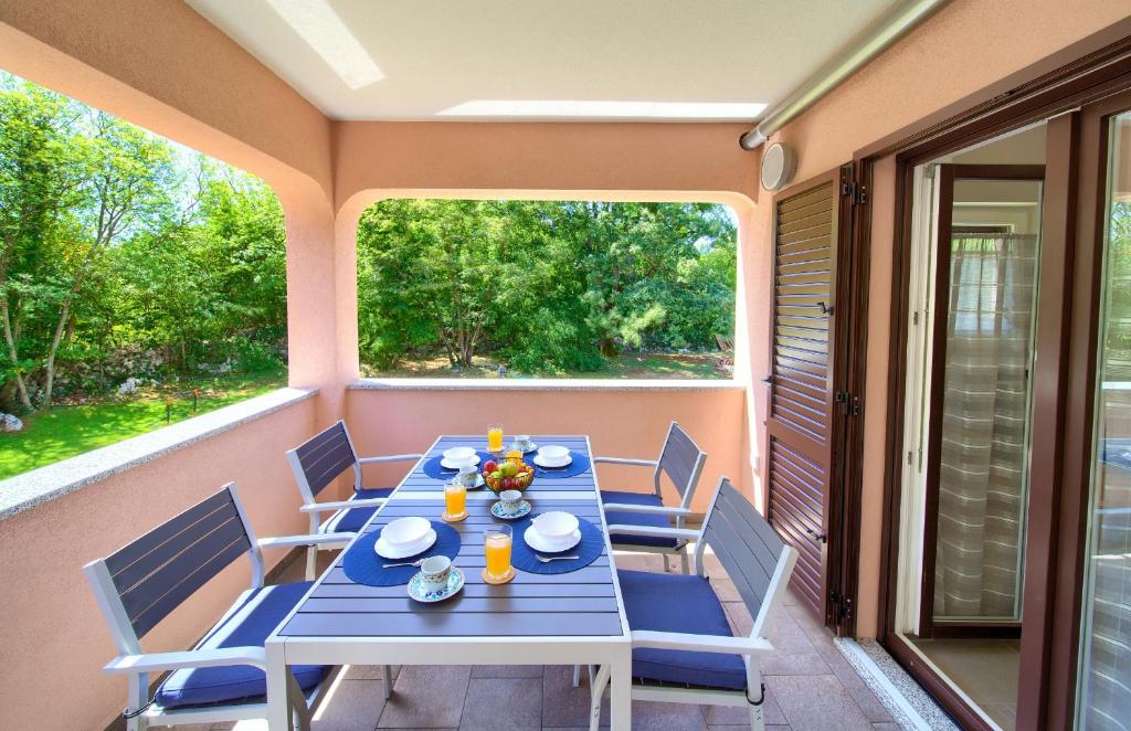 una mesa y sillas en el porche trasero de una casa en Oak Meadow Apartment en Dobrinj