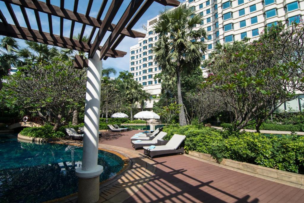 Pool loungers line a landscaped deck beside the hotel tower and a shaded pergola.