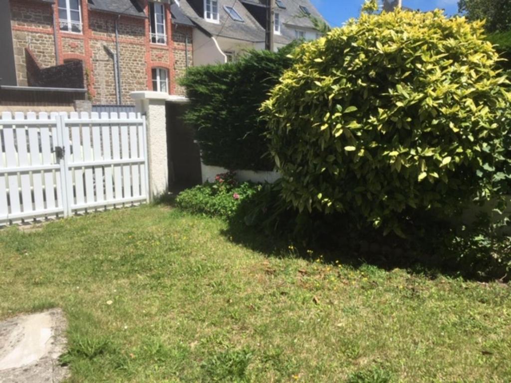 a white fence in front of a yard with a bush at Le Cartier in Saint-Lunaire
