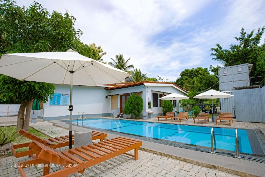 a pool with chairs and umbrellas next to a house at Hotel Le Green Udawalawe in Udawalawe