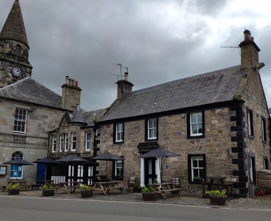 um antigo edifício de pedra com mesas e guarda-sóis em The Covenanter Hotel em Falkland