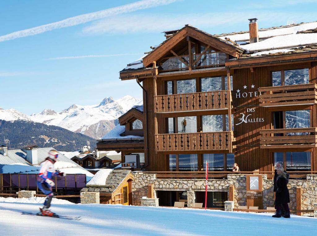 a couple of people skiing in front of a hotel at Les Trois Vallées, a Beaumier hotel in Courchevel