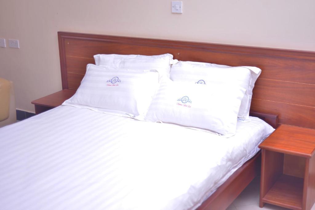 a bed with white pillows and a wooden headboard at Nabisere Hotel Kalisizo in Kalisizo