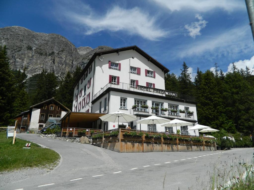 a large white building with umbrellas next to a road at Hotel Preda Kulm in Bergün