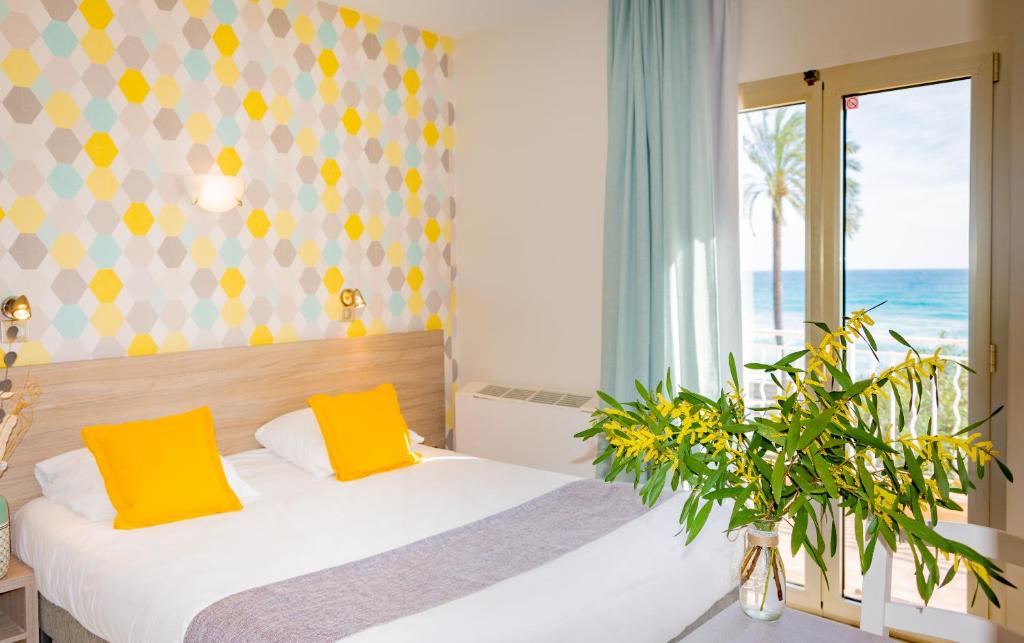 a bedroom with a bed with yellow pillows and a window at Hotel et Appartements Reine D'Azur in Roquebrune-Cap-Martin