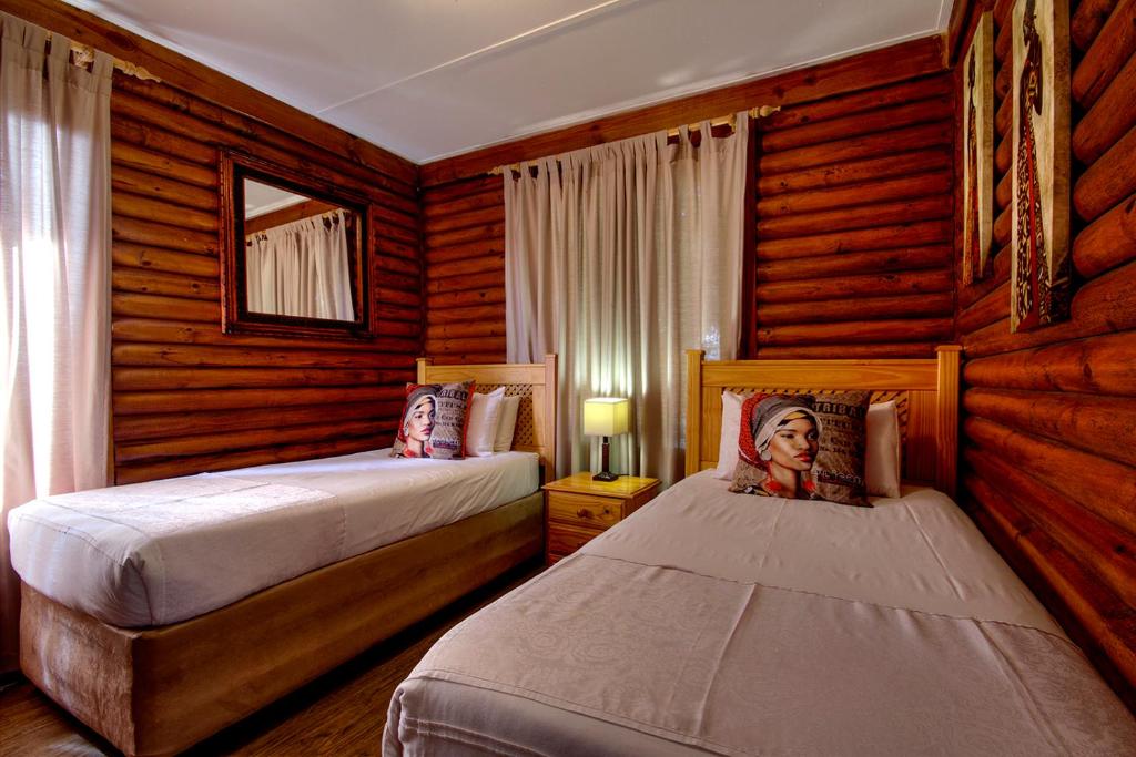 two beds in a bedroom with wooden walls at Sunset Lodge in St Lucia