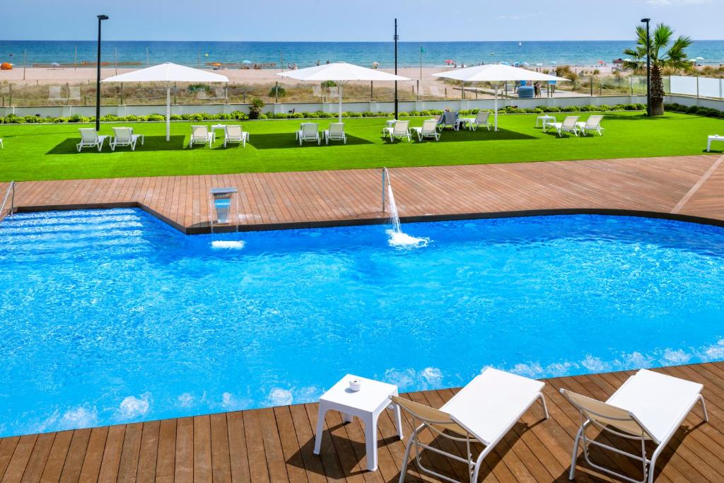 uma piscina com cadeiras e guarda-sóis e a praia em Hotel Playafels em Castelldefels