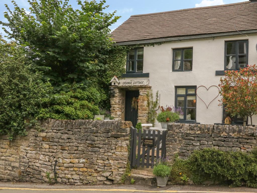 a white house with a stone wall and a fence at Grange Cottage in Castleton