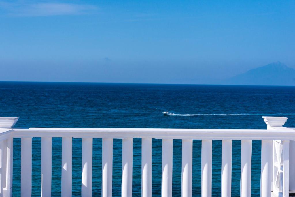 a white fence overlooking the ocean with a boat in the water at Hotel Samaras Beach in Limenaria