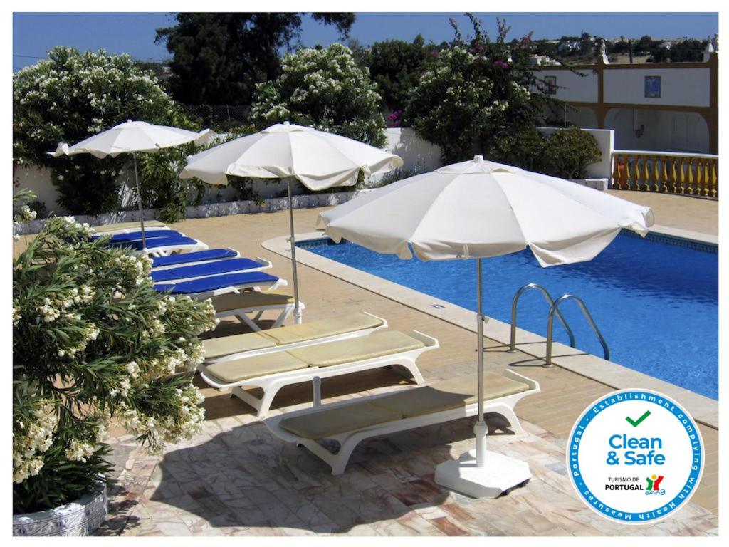 a group of umbrellas and lounge chairs next to a pool at Apartamentos Vivenda Veiguinha in Albufeira
