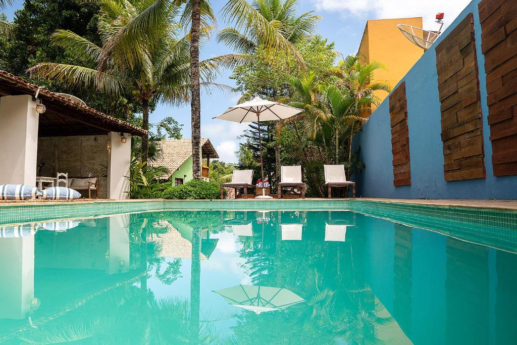 a swimming pool with chairs and an umbrella and palm trees at Calypso INN in Trancoso