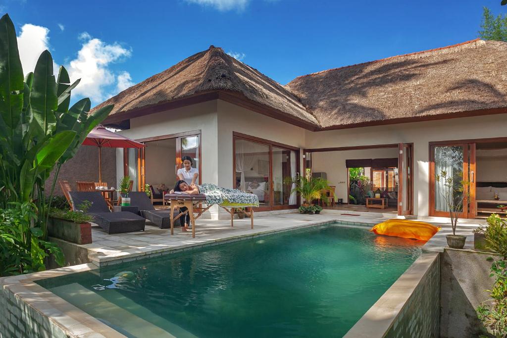 a villa with a swimming pool in front of a house at Anusara Luxury Villas in Ubud