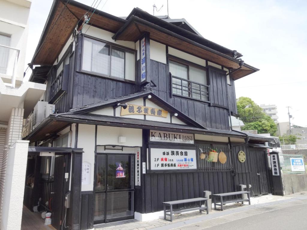 ein schwarzweißes Gebäude mit zwei Bänken davor in der Unterkunft Minshuku Inn Shirahama Uminoyado in Shirahama