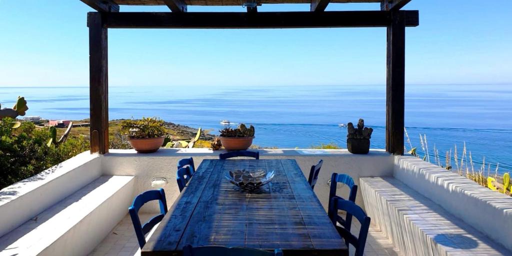 eine Terrasse mit einem Tisch, Stühlen und Meerblick in der Unterkunft Dammusi A- Mare Pantelleria in Pantelleria
