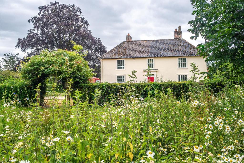 an old white house behind a field of flowers at Grove Farm House in Thornham Magna