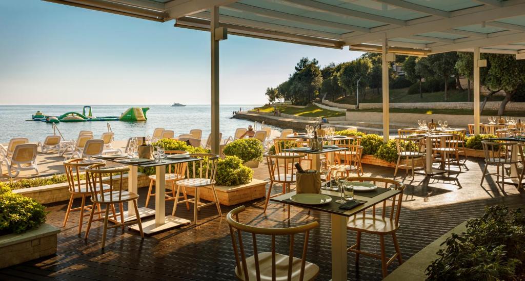 ein Restaurant mit Tischen und Stühlen neben dem Wasser in der Unterkunft Maistra Select Petalon Resort in Vrsar